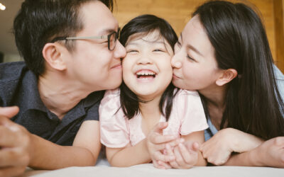 Asian parents kissing their daughter on both cheeks.