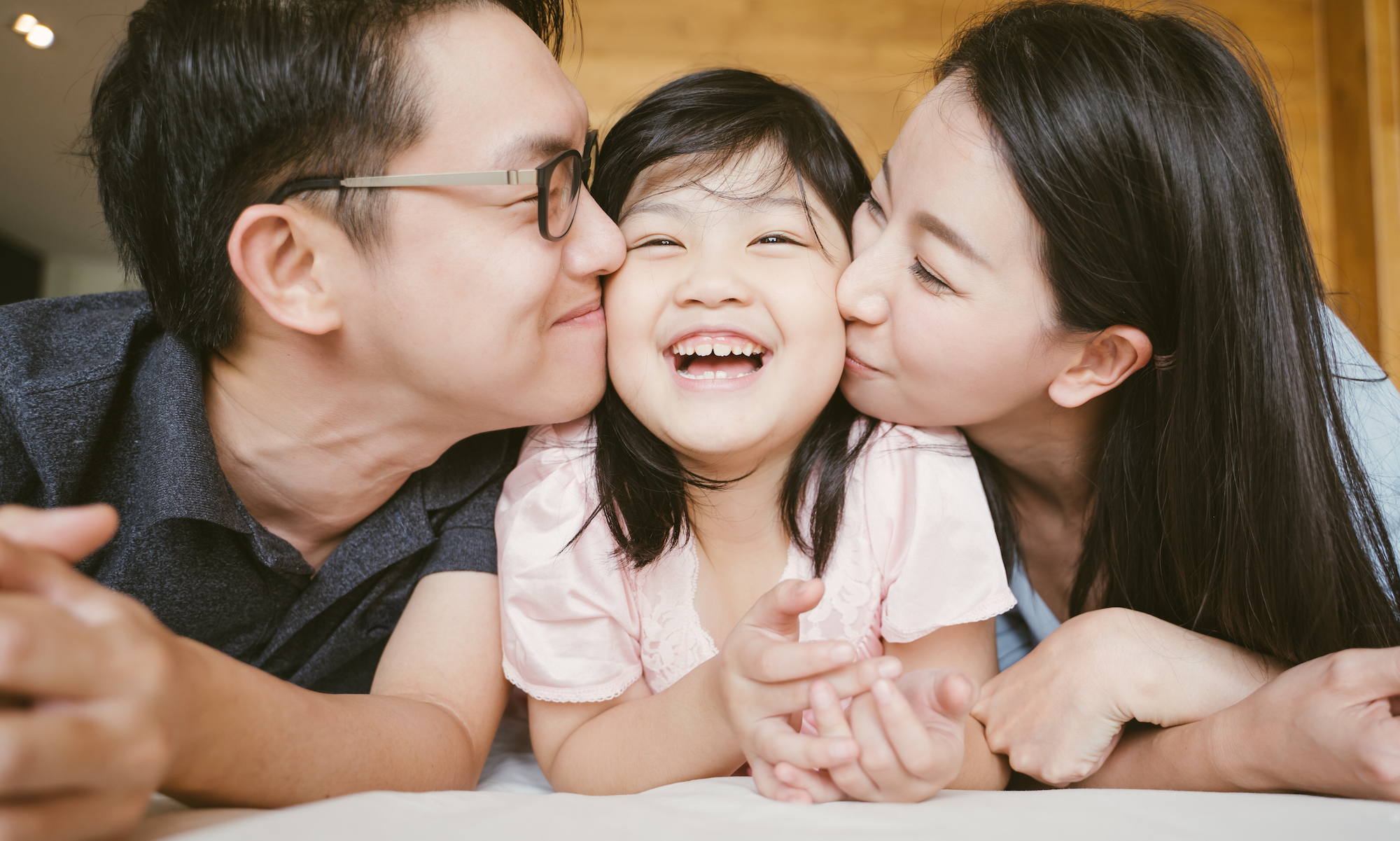 Asian parents kissing their daughter on both cheeks.