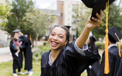 A young female graduate smiles at the camera while holding her mortarboard