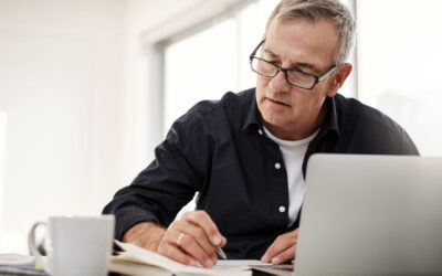 Man on laptop at desk checking papers